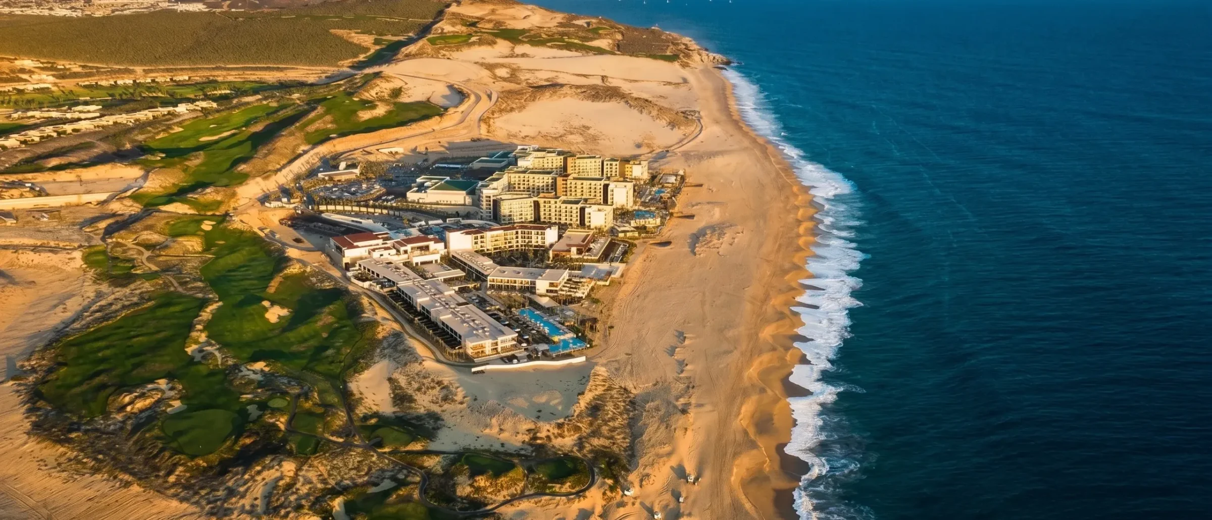 Aerial view of a beachfront resort beside golf fairways and sand dunes along the deep blue Pacific coastline