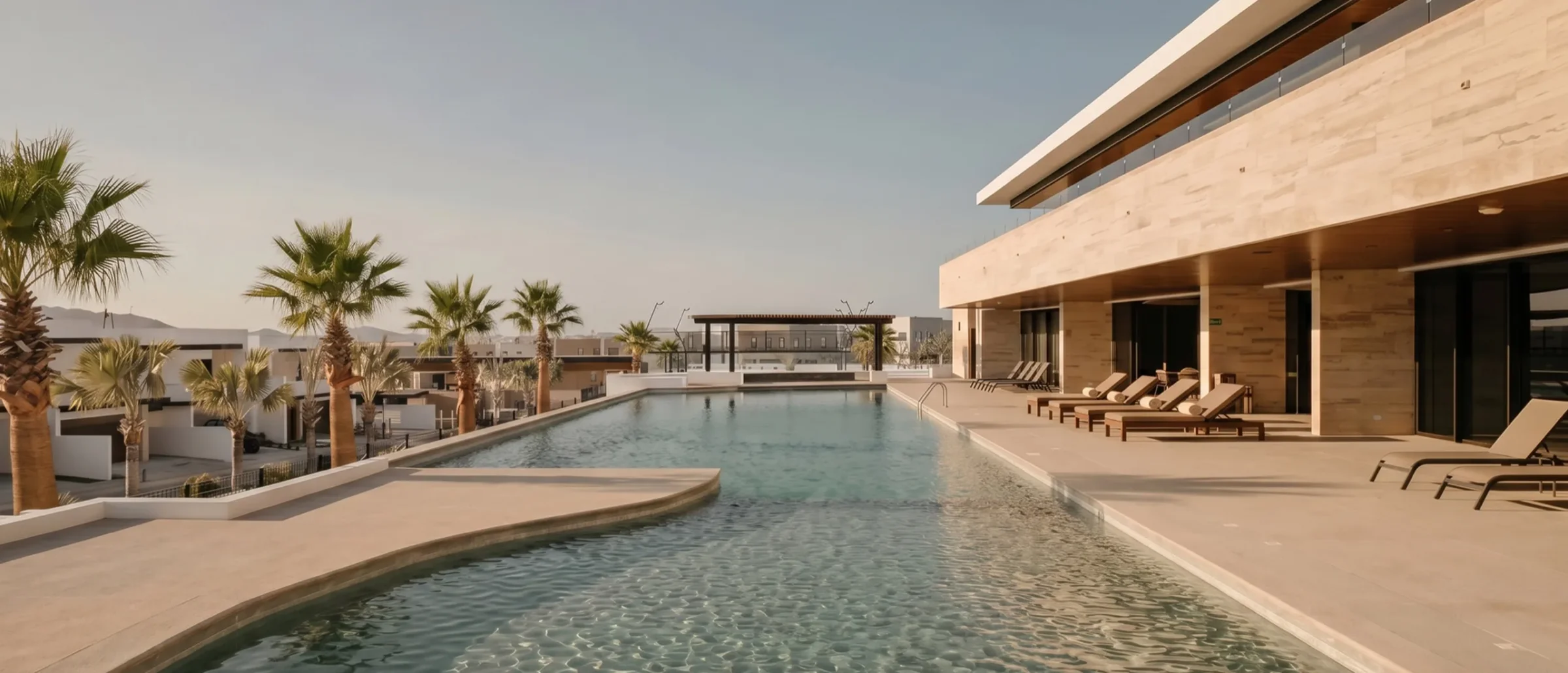 Long pool beside a stone-clad clubhouse with lounge chairs and palm trees in El Tezal
