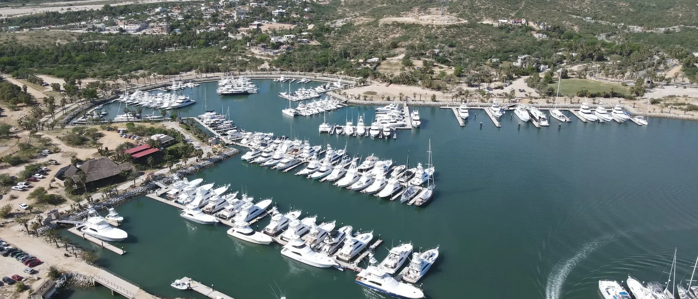 Aerial view of a marina with rows of white yachts at floating docks, with desert hills and mountains behind