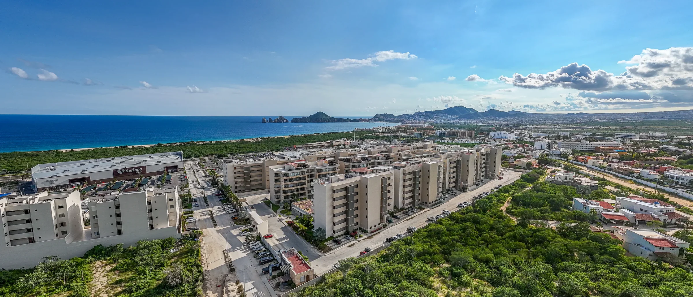 Aerial view of mid-rise condos and desert scrub near the coast, with the Land's End rock arch in the distance